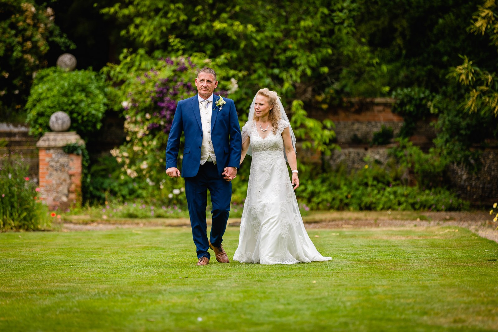 The couple walking hand in hand across the lawns at Grim's Dyke Hotel
