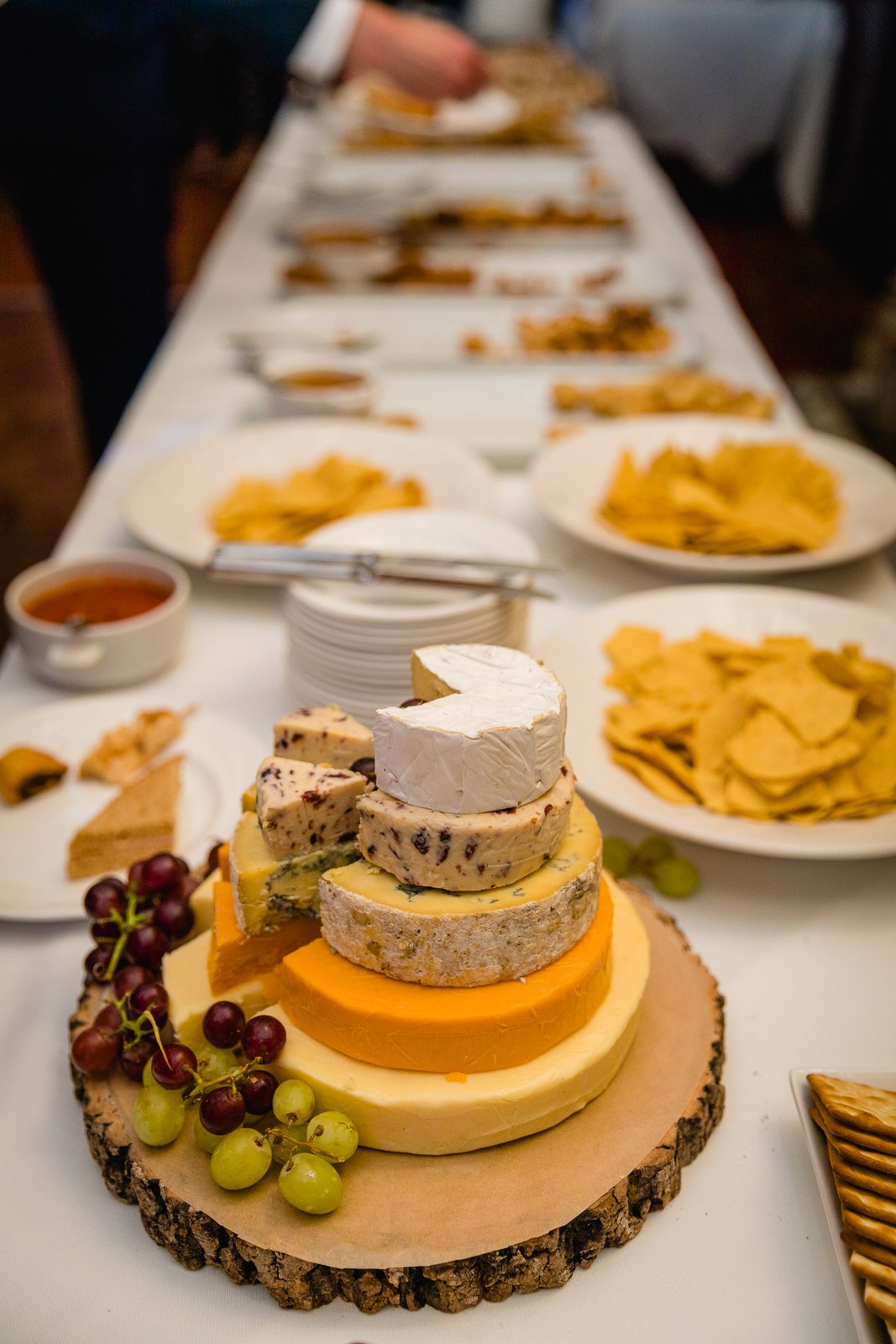 A grazing table of stacked cheese wheels, grapes and crackers