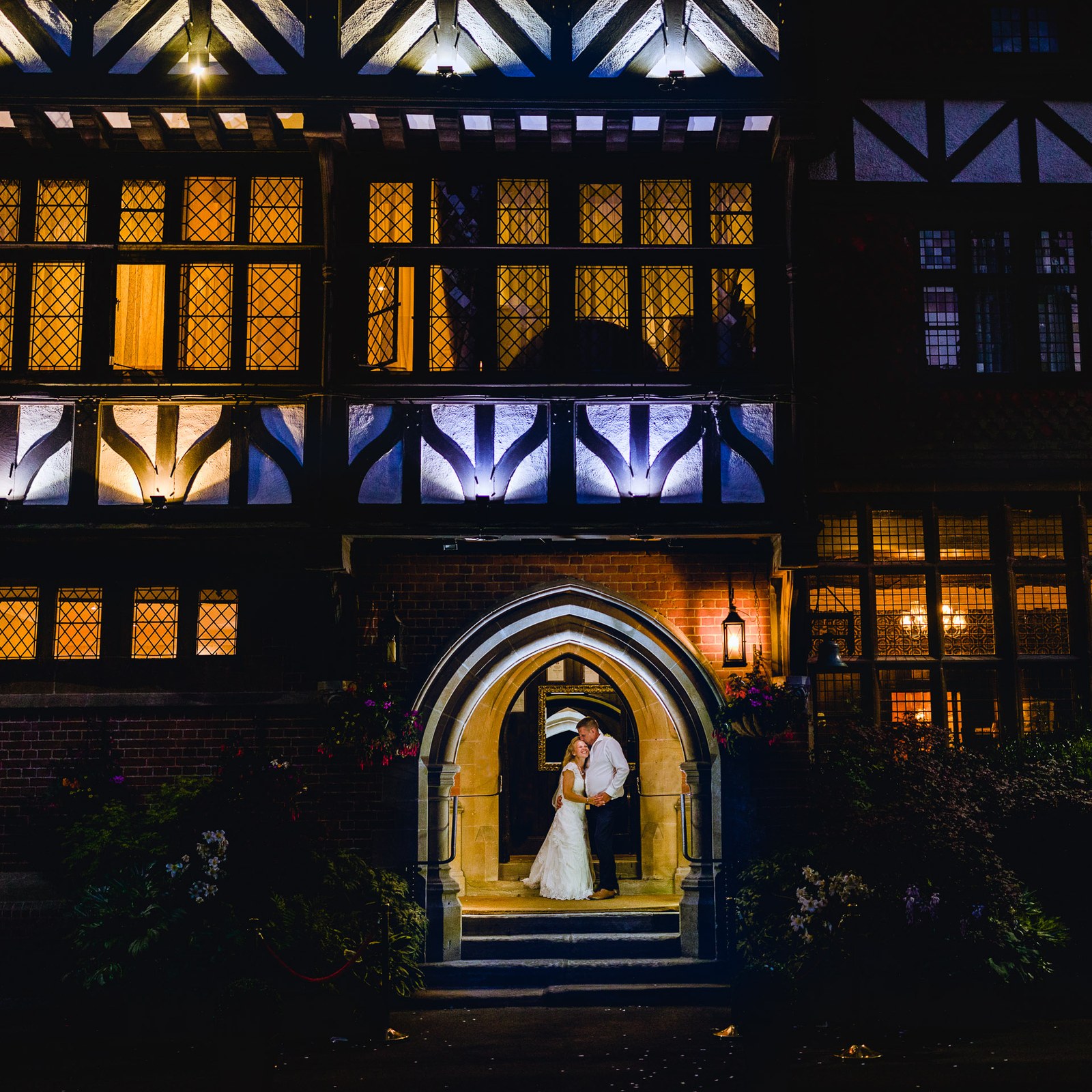 The timber-framed house at Grim's Dyke Hotel floodlit at night, the couple in the lit archway
