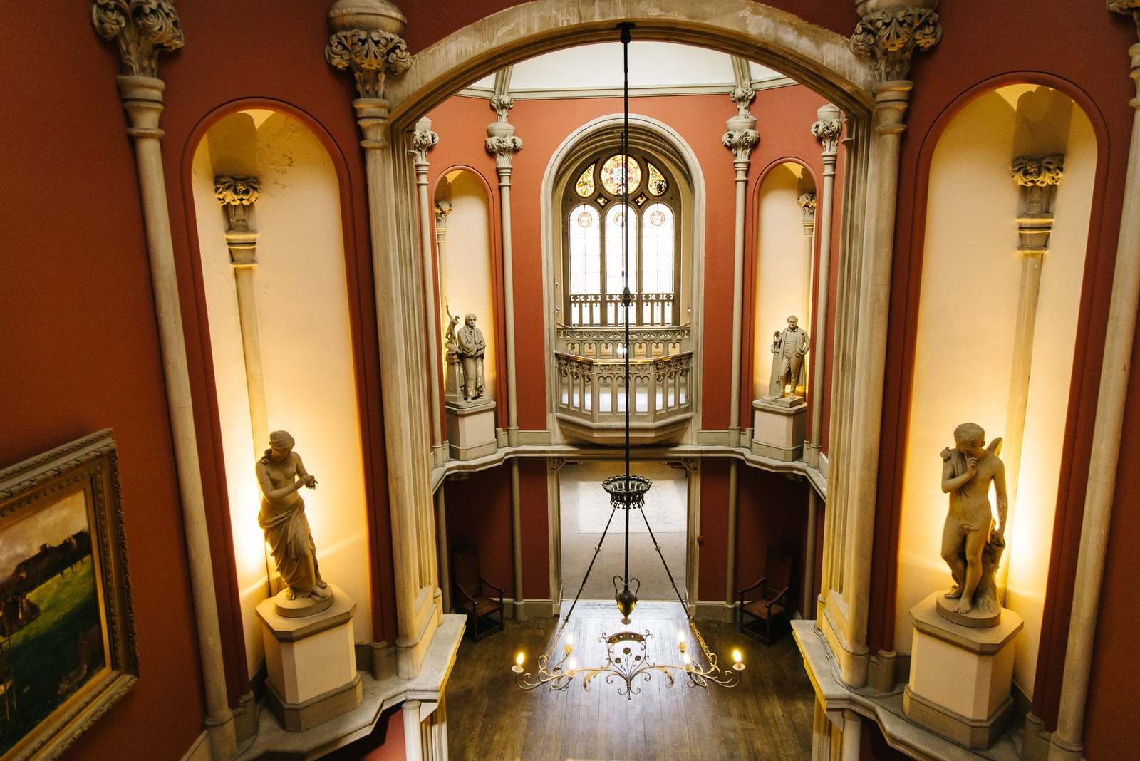 The galleried hall at Grittleton House, statues set in arched niches beneath a chandelier and terracotta walls