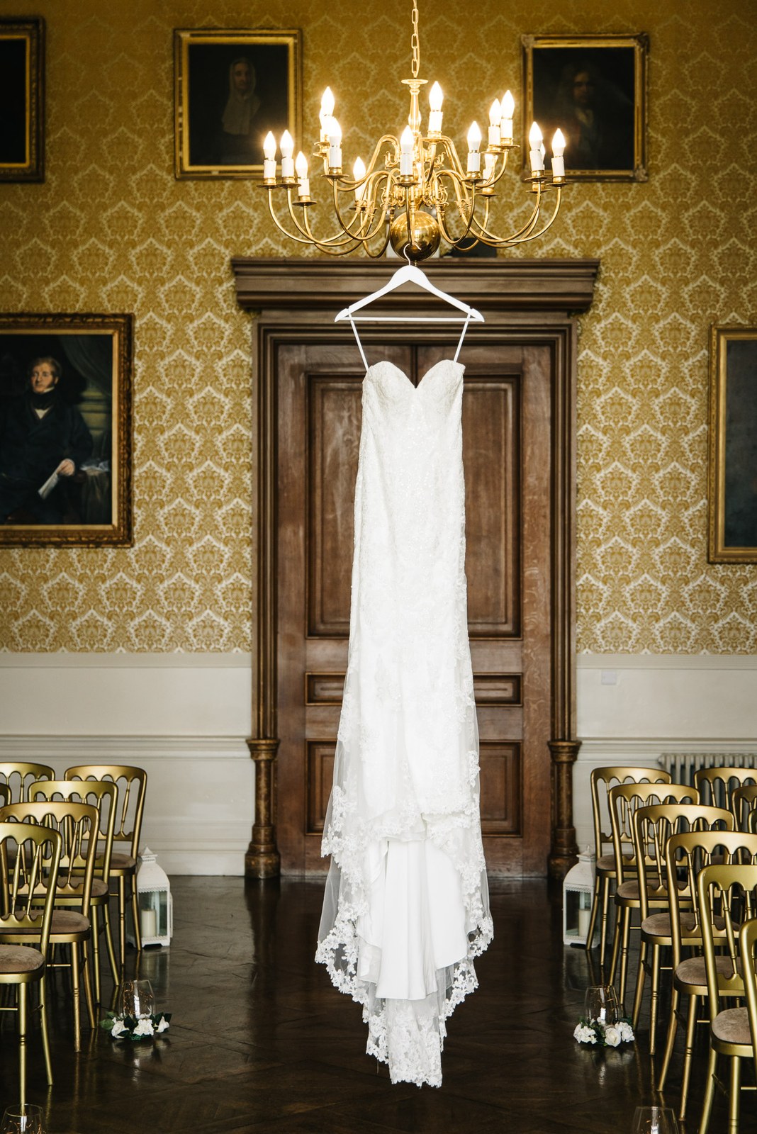 The bride's lace gown hanging on a panelled door in the damask-walled ceremony room