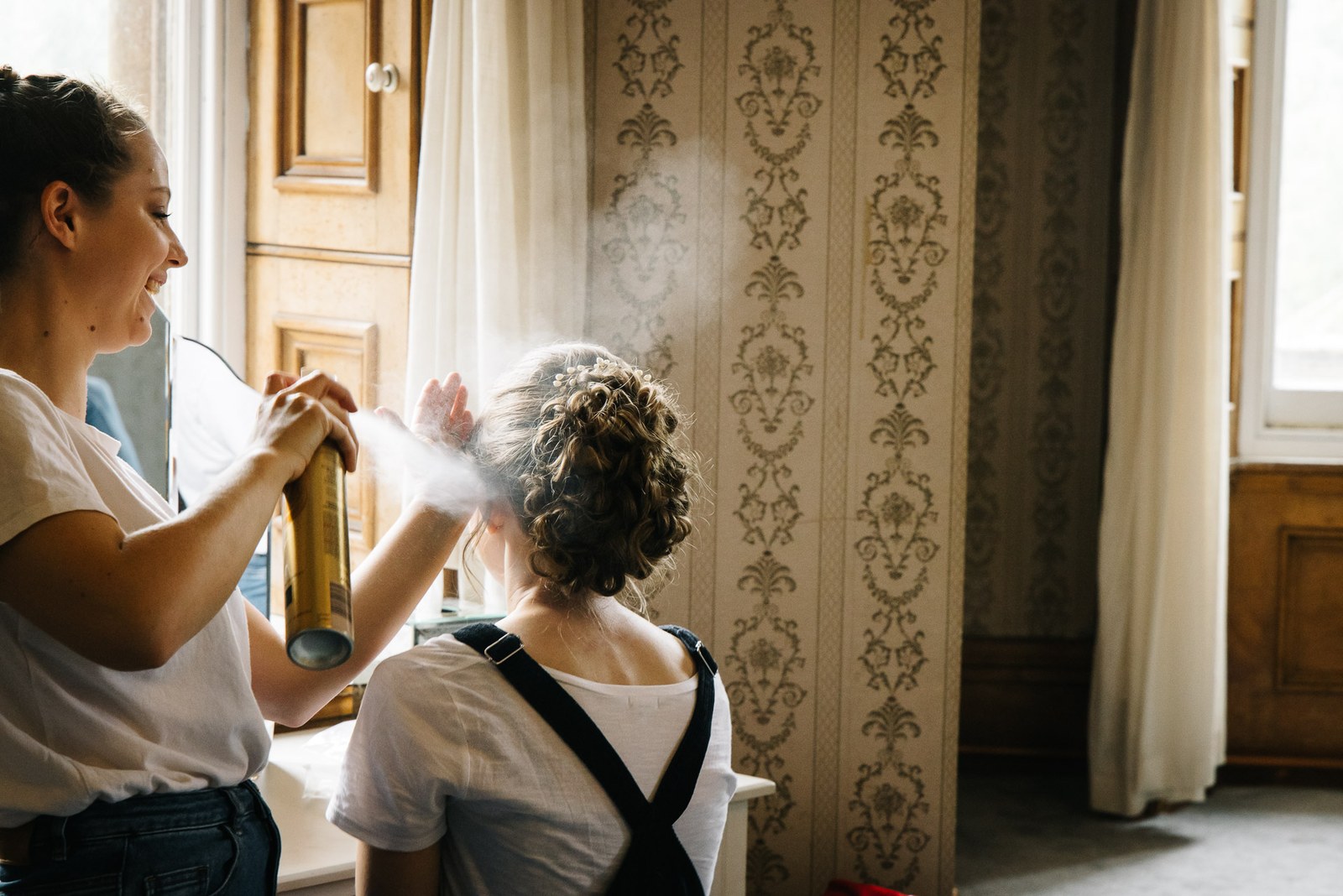A stylist spraying a curled updo into place during the morning preparations