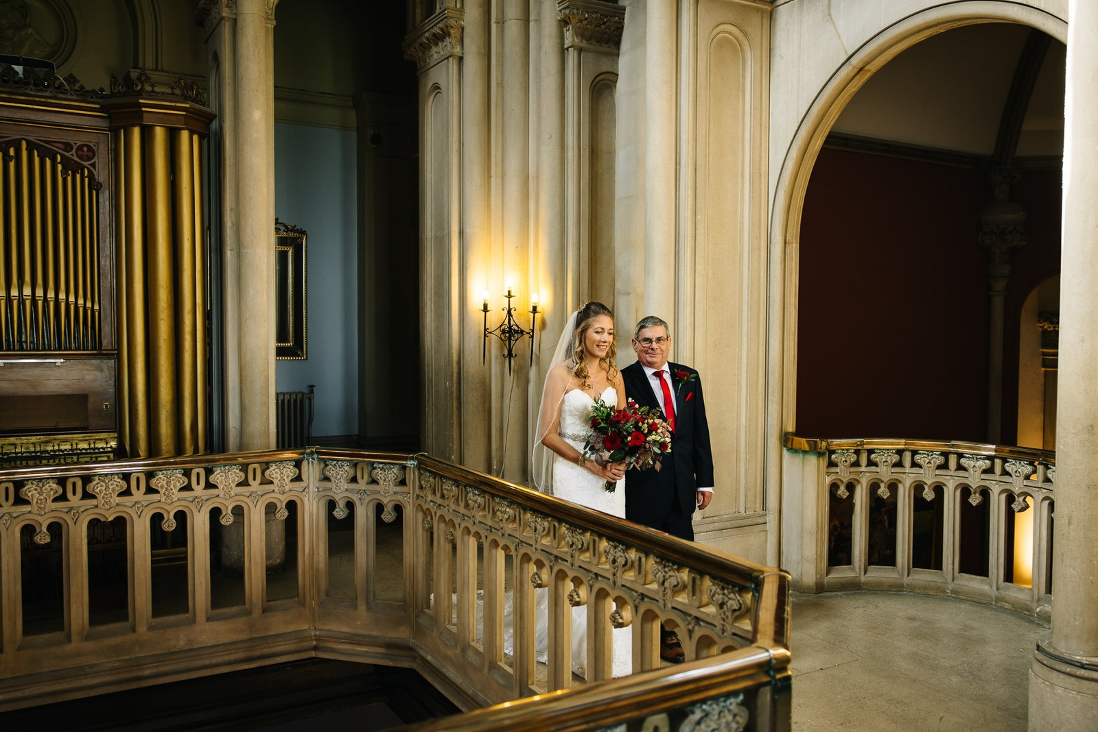 Bride and her father pausing on the staircase beside the organ pipes at Grittleton House