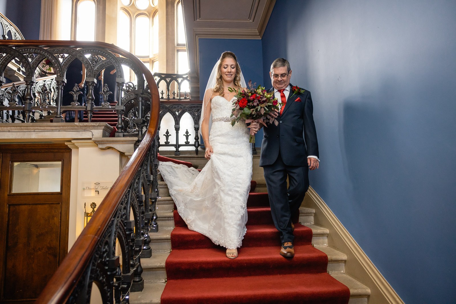 Bride and her father descending the grand red-carpeted staircase at Grittleton House