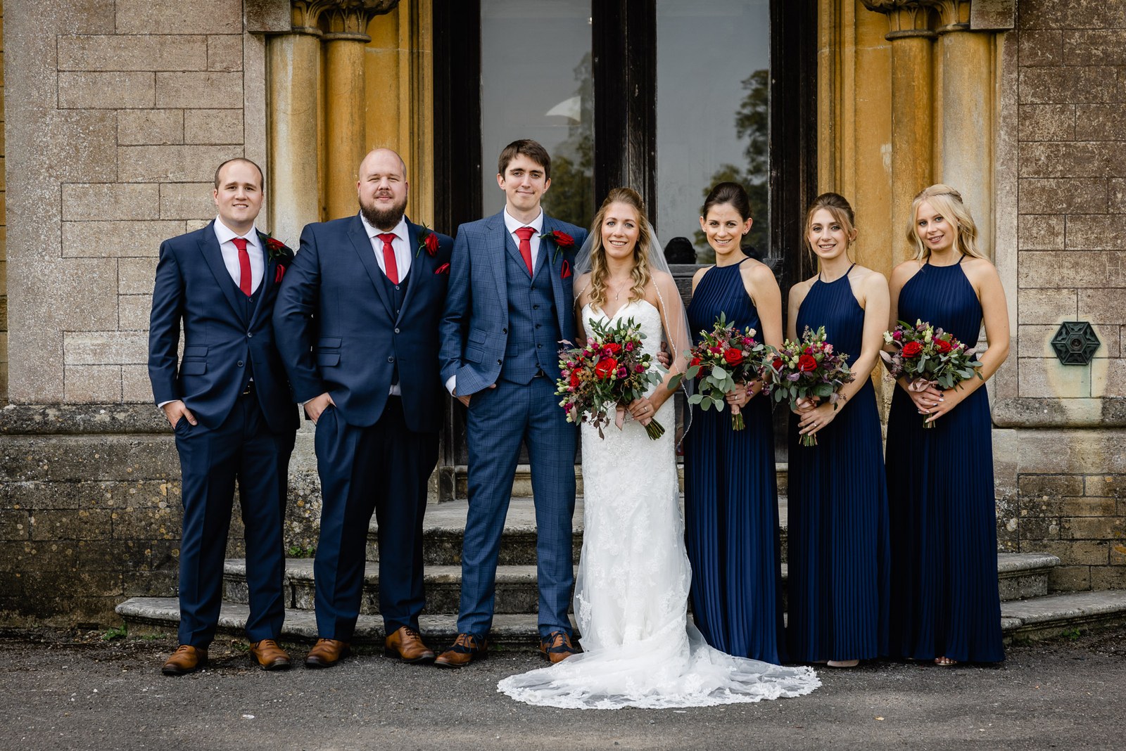 The bridal party gathered on the stone steps, bridesmaids in navy with red bouquets
