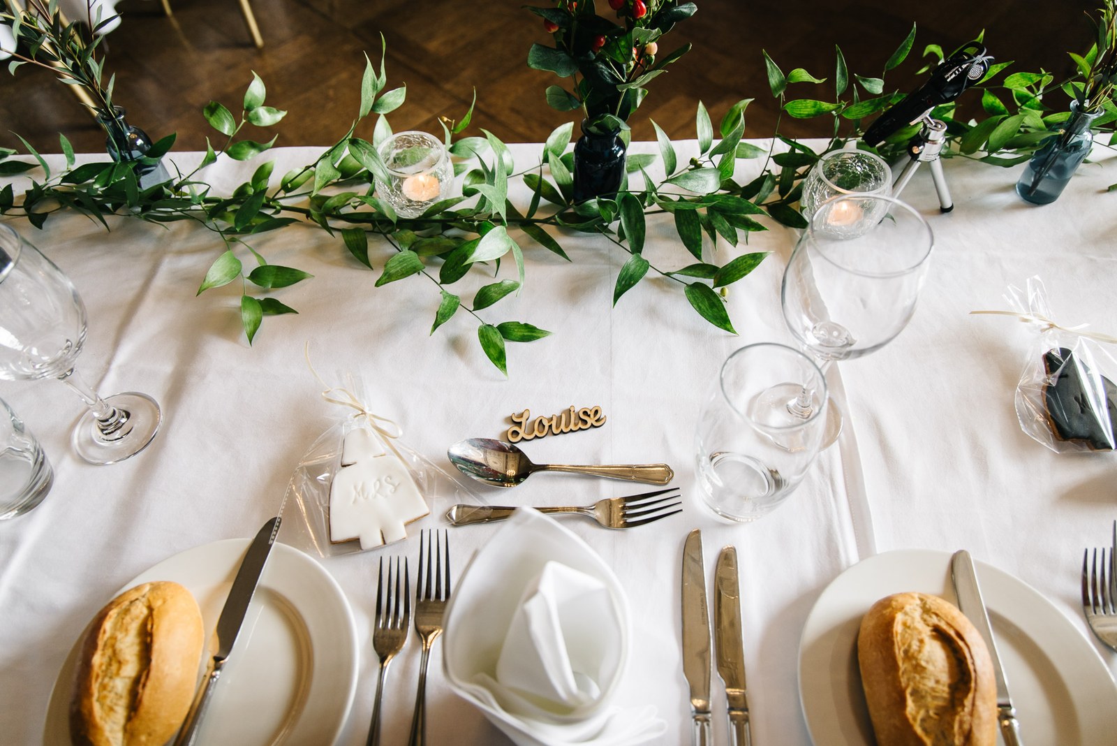 Close-up of a place setting with a foliage garland, glassware and a guest name card