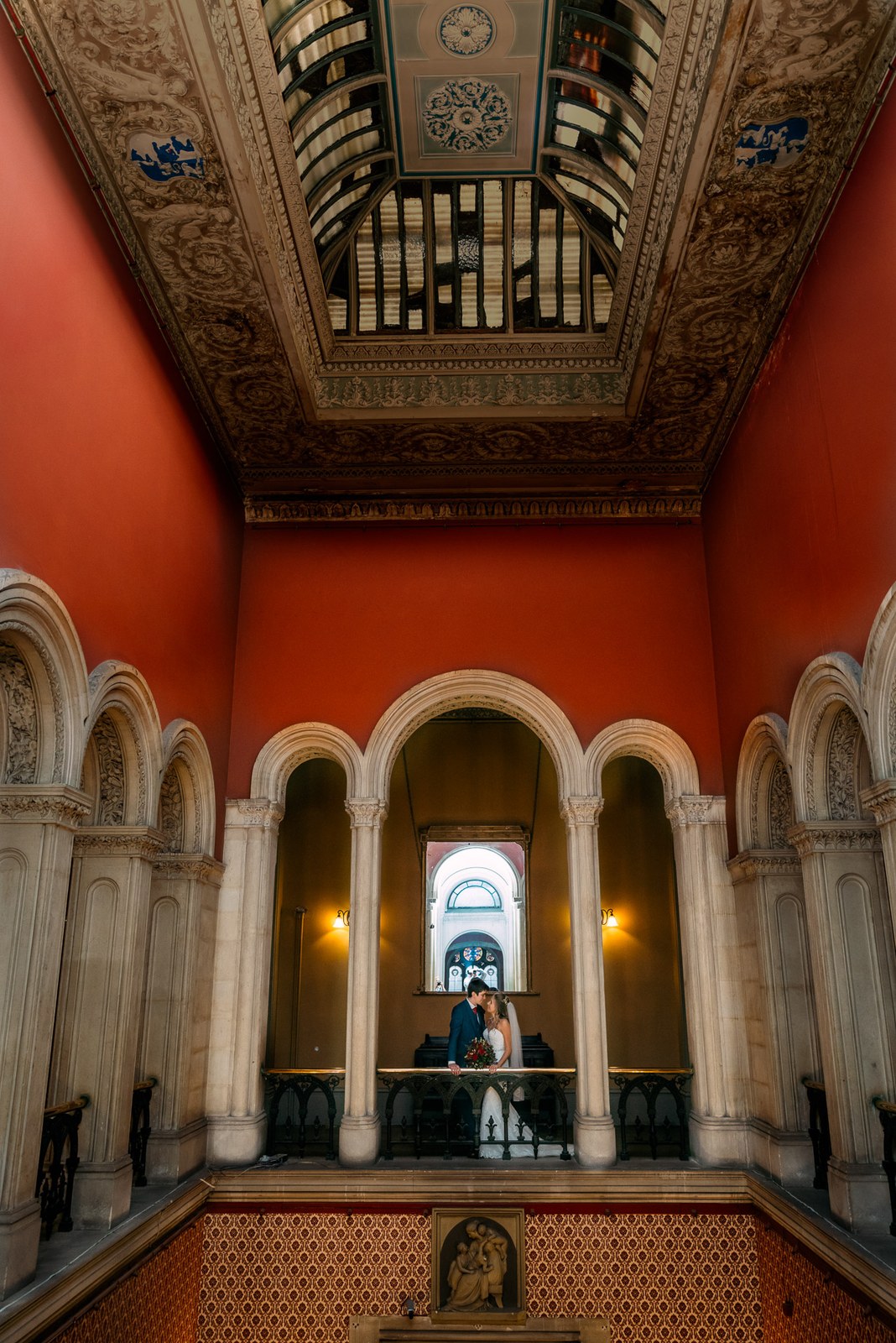 The couple small within the towering red-walled hall and its gilded ceiling at Grittleton House