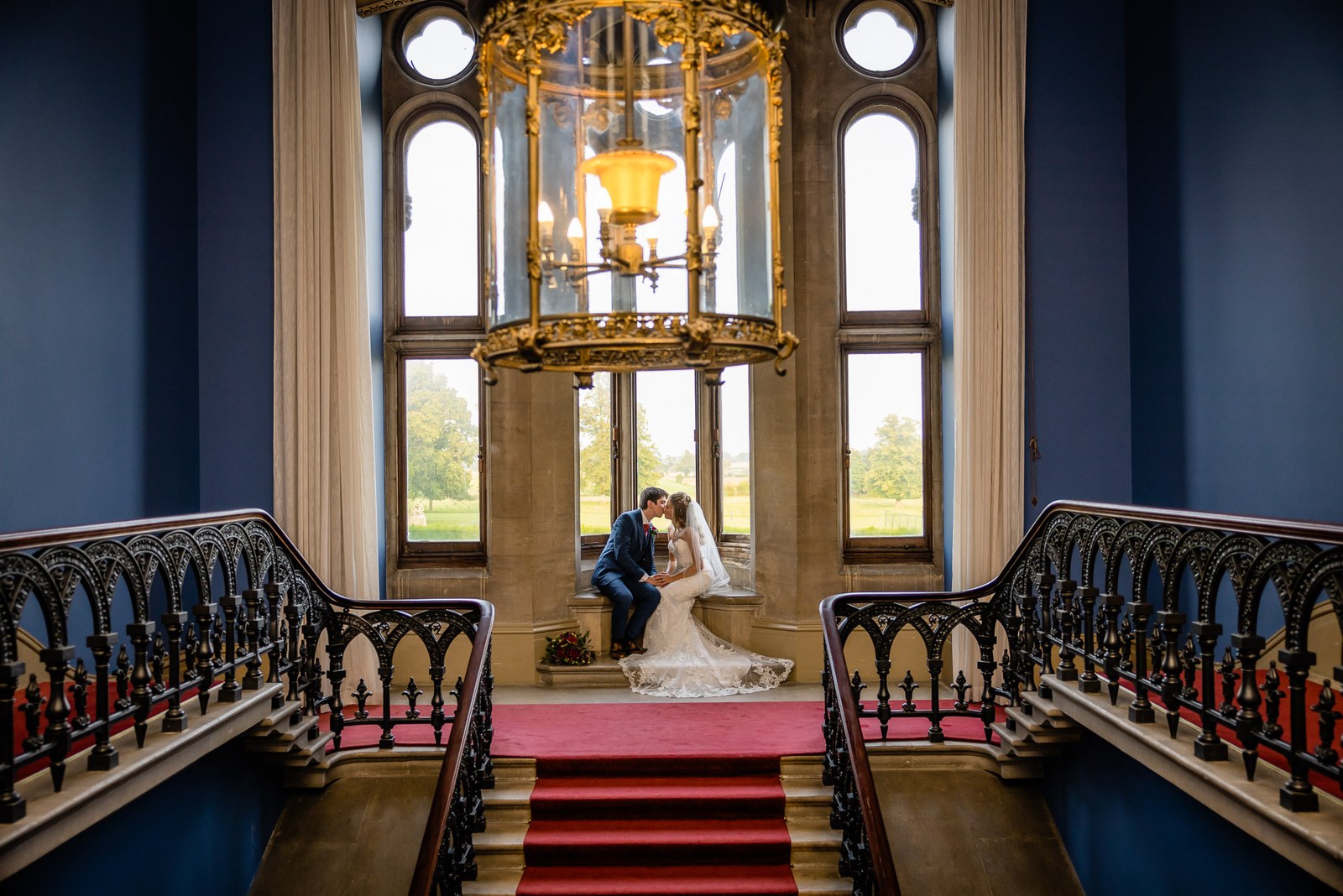 Newlyweds kissing on the grand staircase landing beside a lantern and red carpet