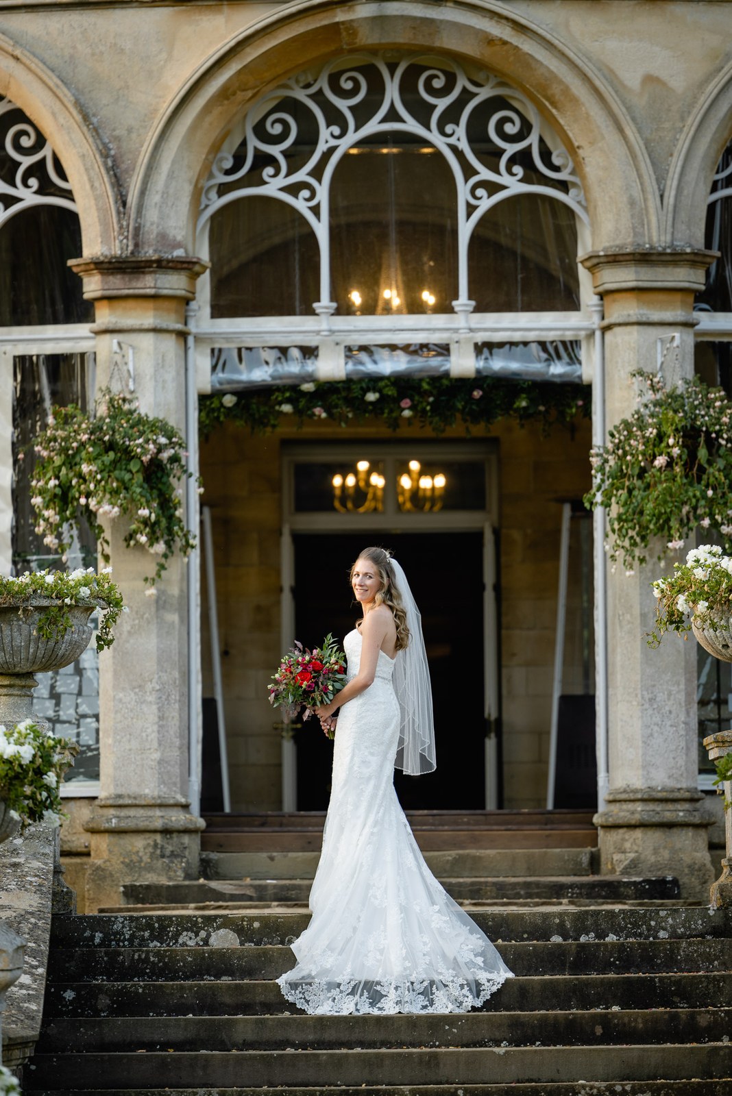 Bride on the stone steps beneath the glazed arched portico, veil trailing