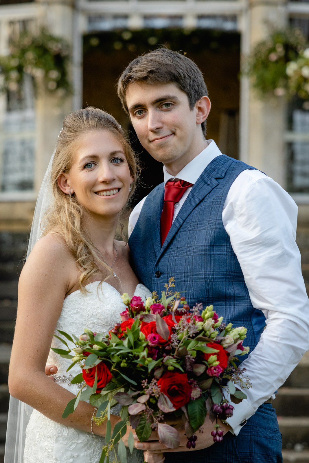 Close portrait of the newlyweds, the bride holding a rich red rose bouquet