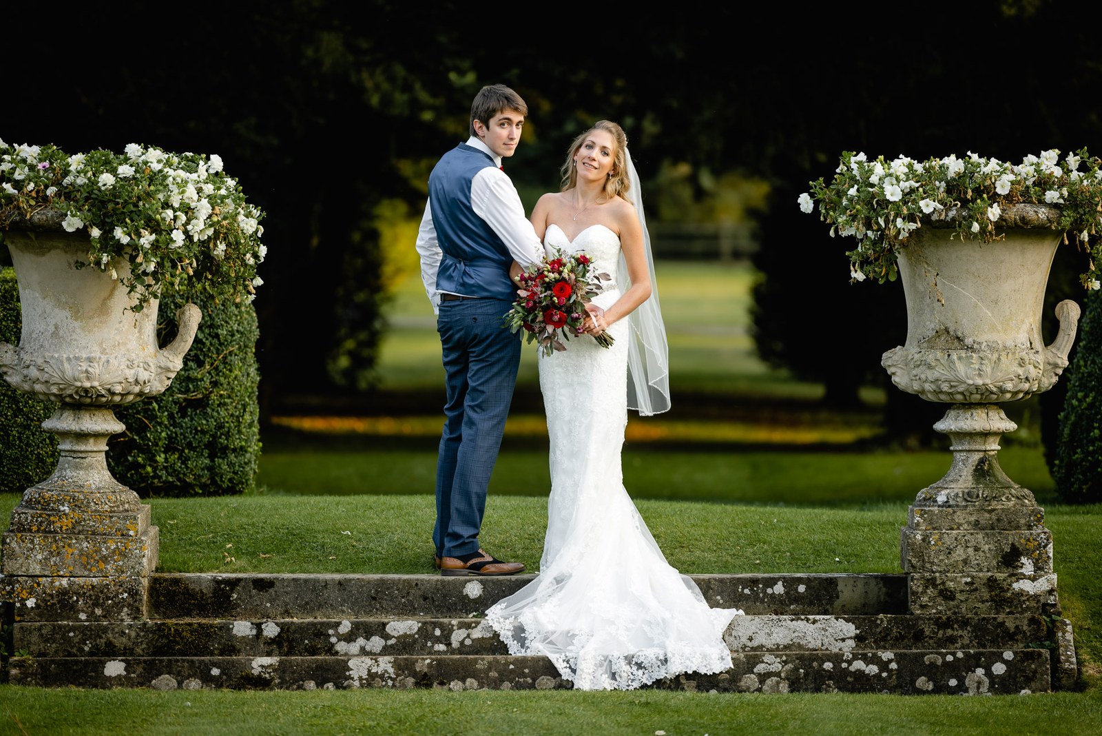 The couple posed between weathered stone garden urns on the lawn