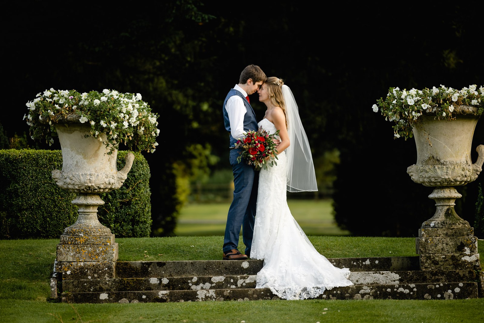 The couple sharing a quiet moment between planted stone urns at twilight