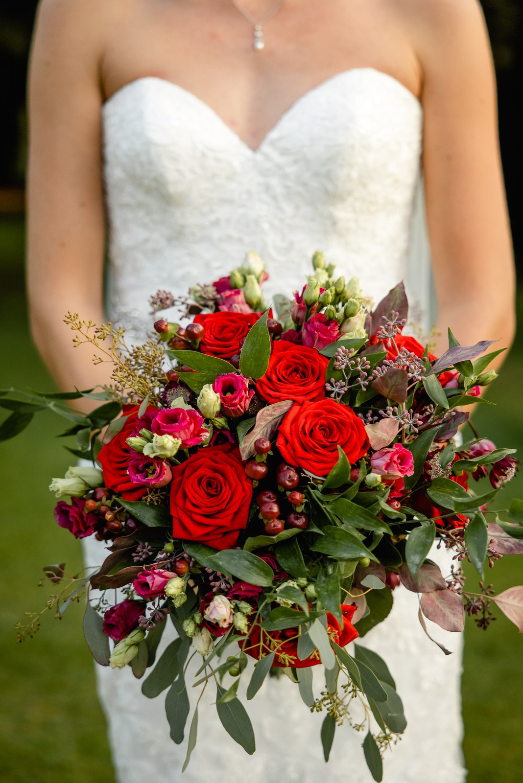 Close-up of the bride cradling a lush bouquet of red roses and foliage