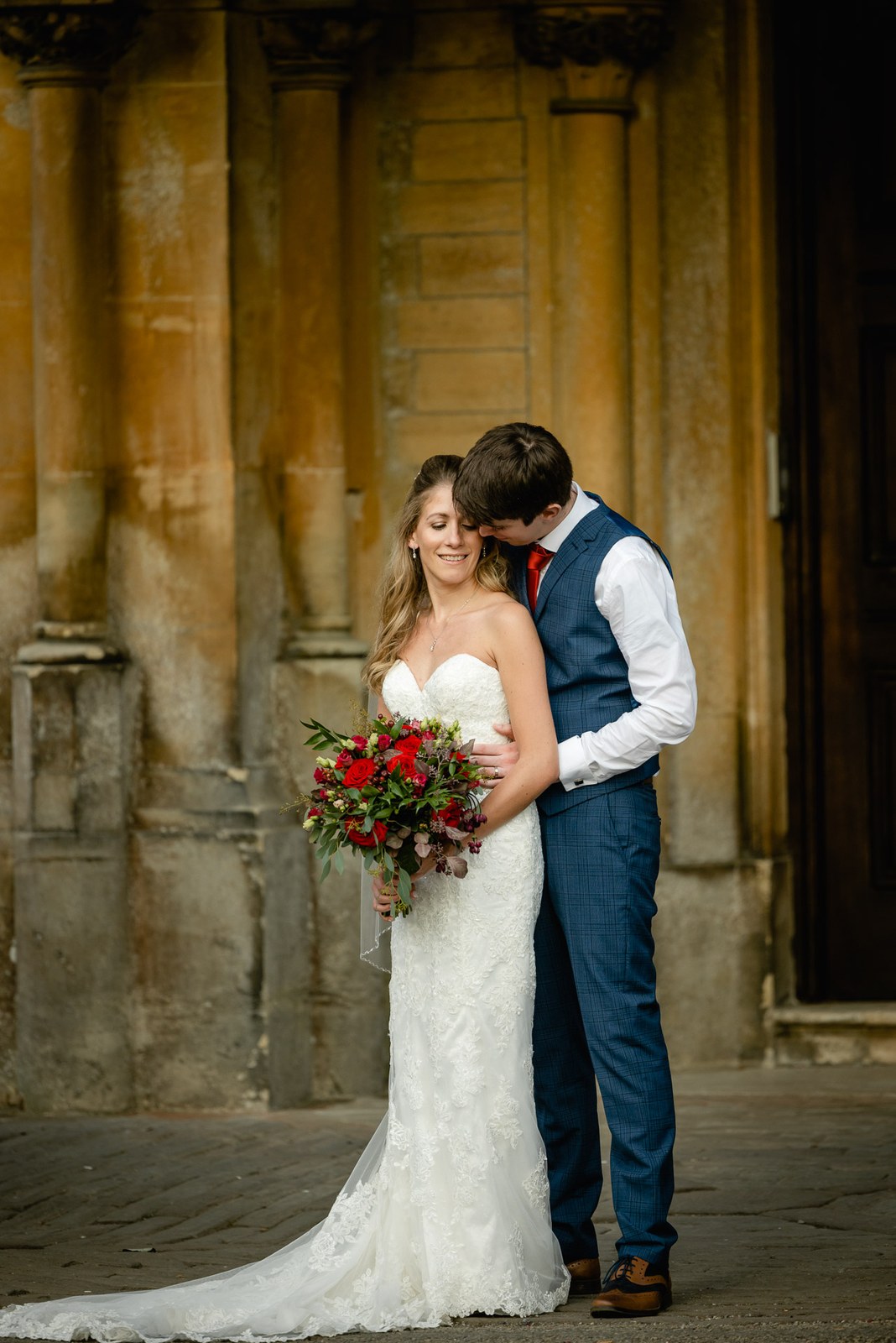 The couple embracing beneath the stone columns of the house at dusk