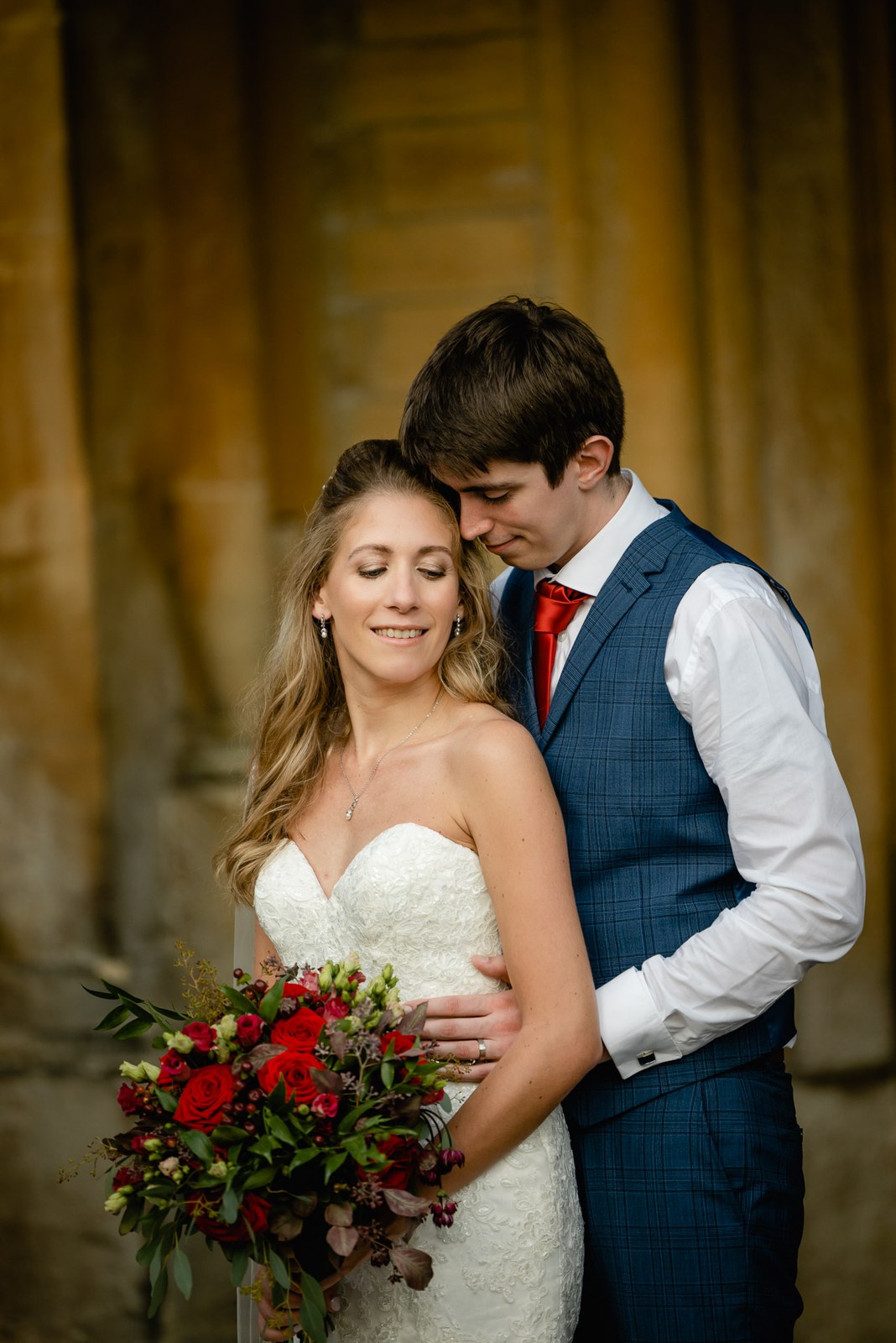 Groom resting his face against the bride's hair in the shadow of the stone colonnade