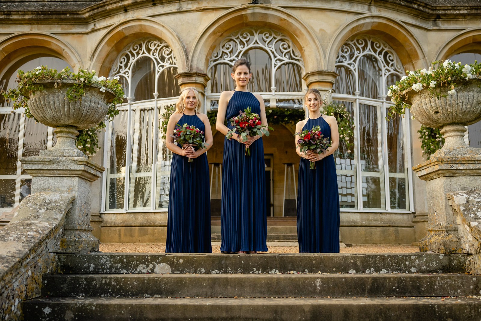 Three bridesmaids with bouquets on the steps below the glazed orangery windows