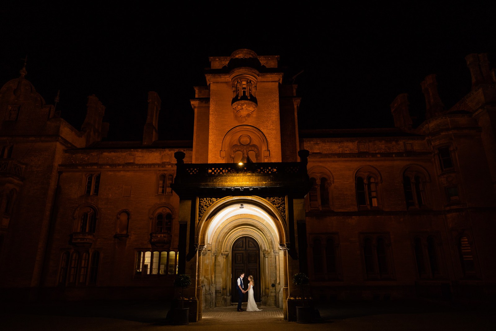 The couple silhouetted in the floodlit stone archway of Grittleton House at night