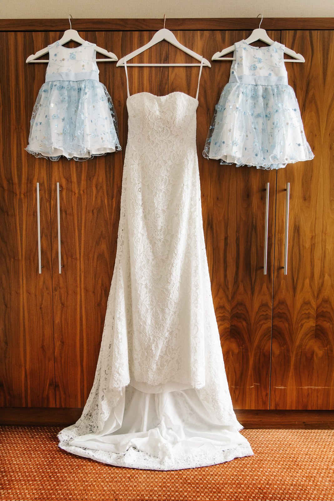 Bridal gown hanging on a wardrobe between two pale-blue flower-girl dresses