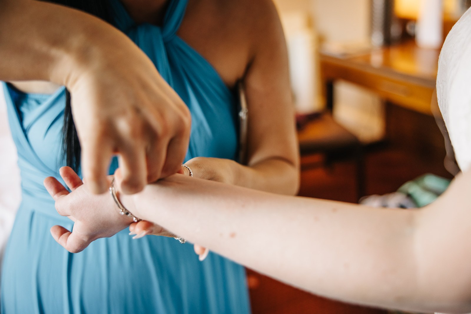 A bridesmaid in teal fastening a bracelet around the bride's wrist