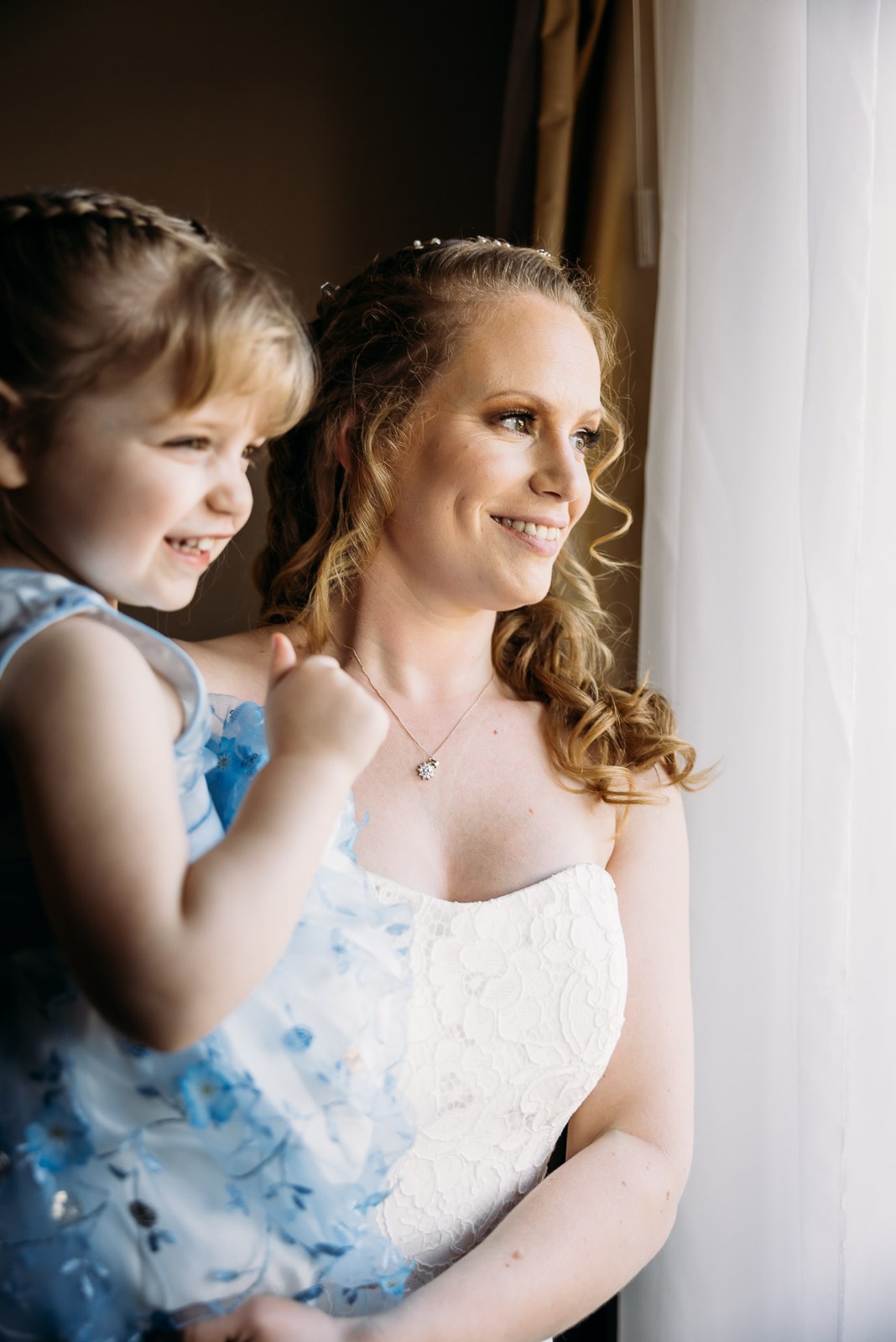 The bride and a young flower girl smiling together by the window