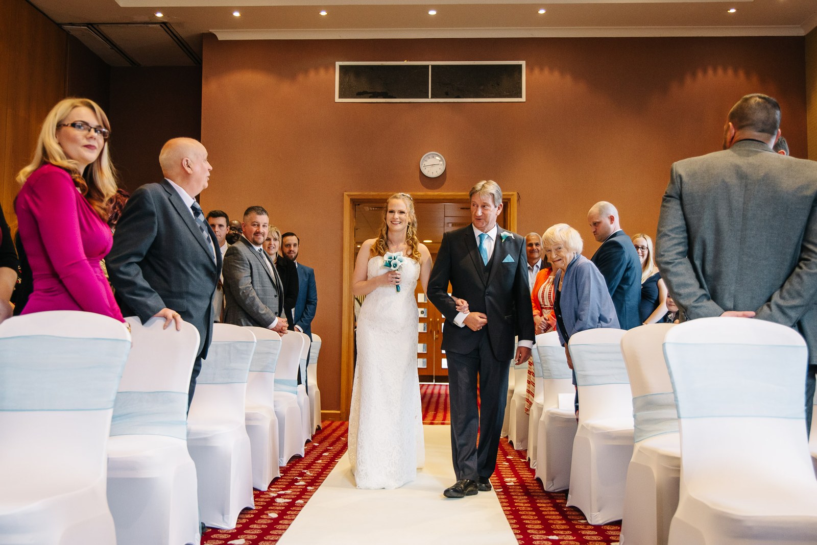 The bride walking down the aisle with her father in the ceremony room at The Hampshire Court Hotel