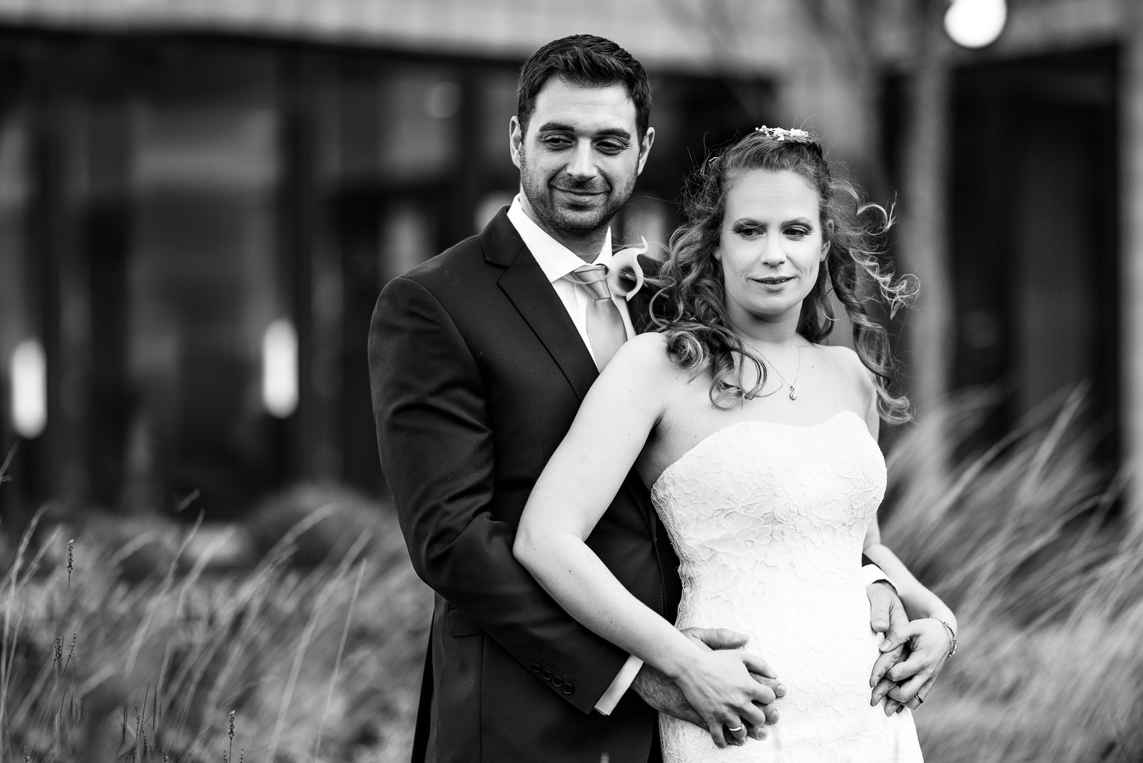 Black and white portrait of the couple embracing among tall ornamental grasses