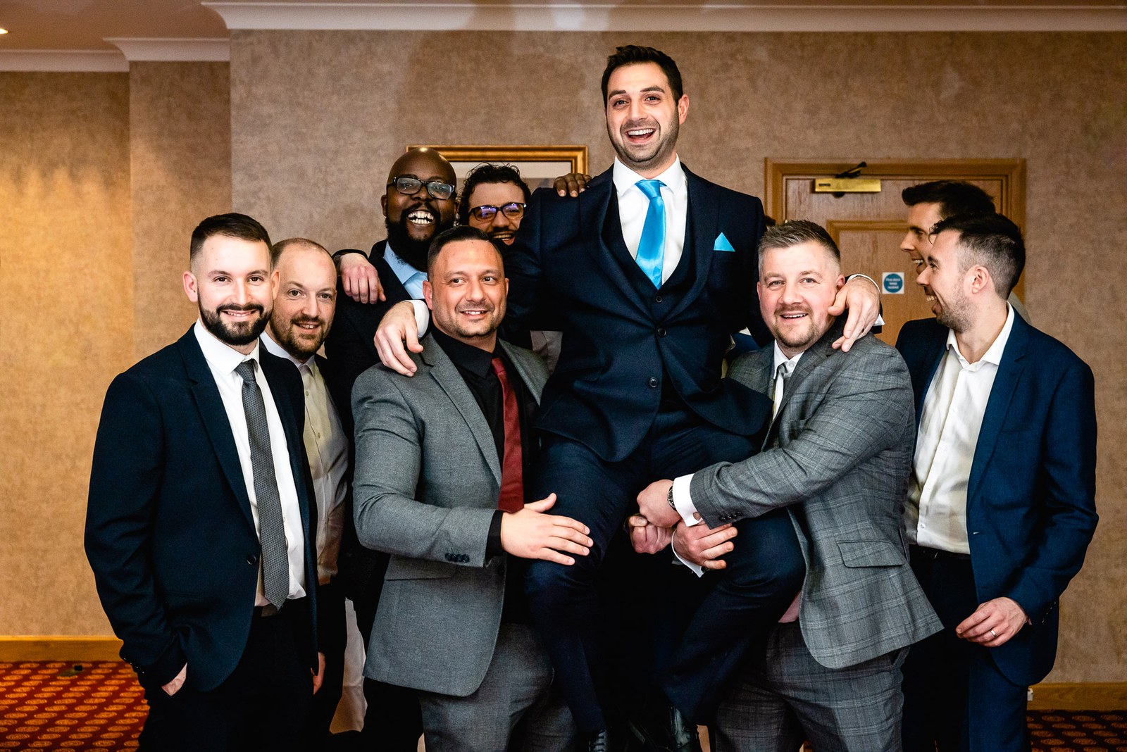 Male guests laughing as they lift the groom off his feet