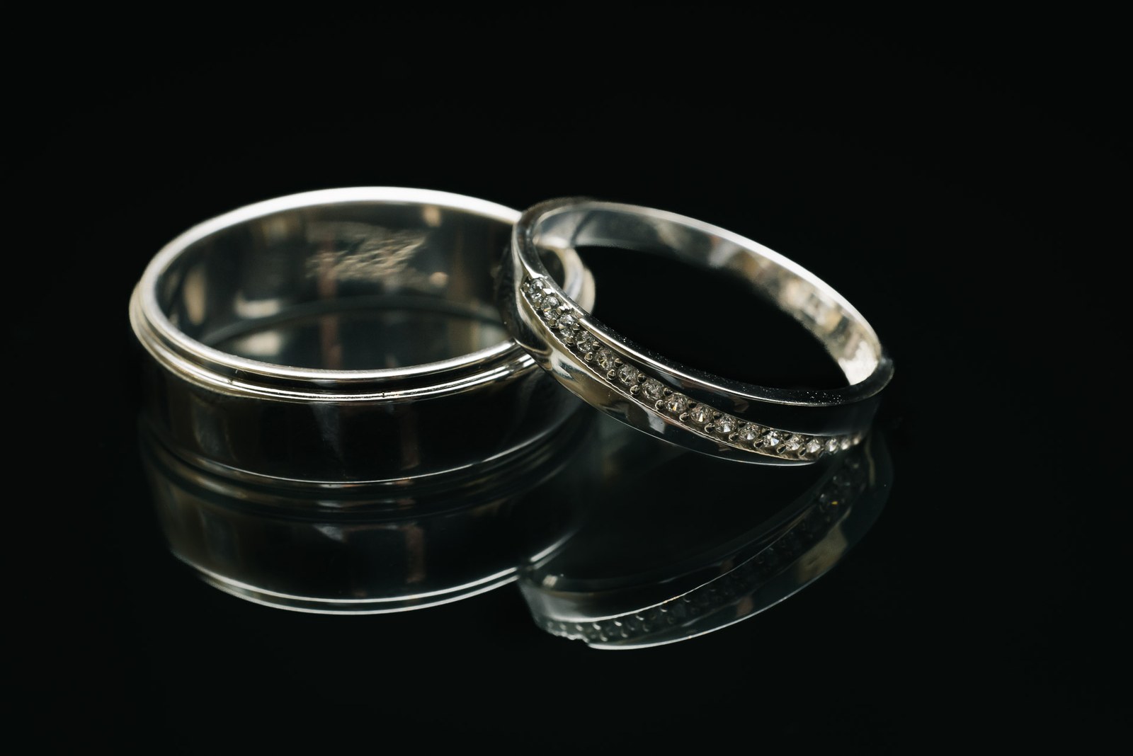 Close-up of two wedding rings, one set with diamonds, on a dark reflective surface
