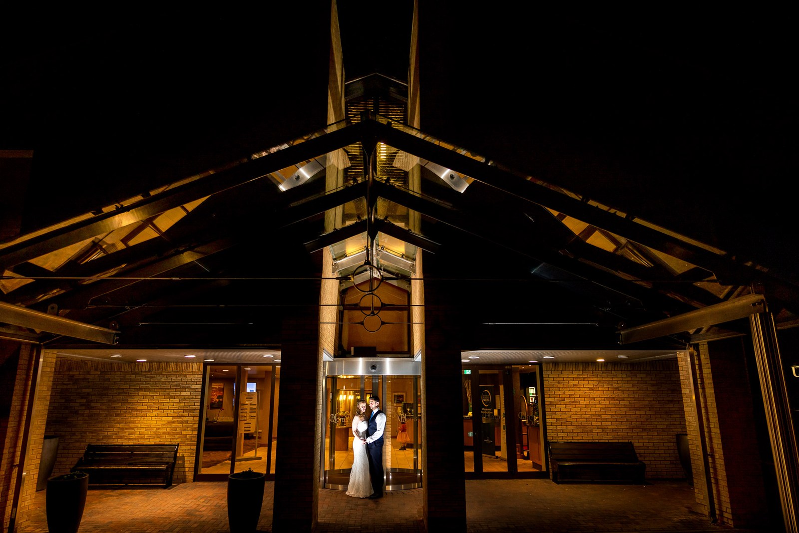 The newlyweds embrace beneath the illuminated apex entrance of The Hampshire Court Hotel at night