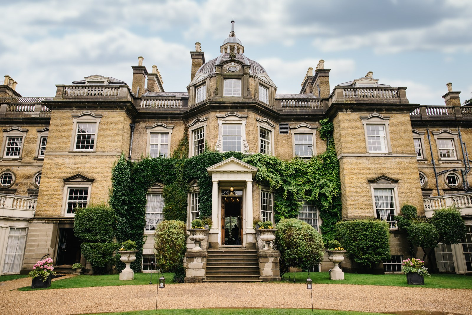 The ivy-clad Georgian frontage of Hampton Court House, crowned by its cupola above a manicured lawn