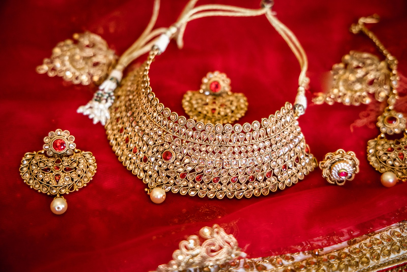 An ornate gold bridal jewellery set with necklace, earrings and maang tikka laid on red velvet