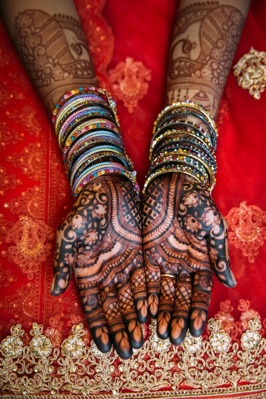 Close-up of the bride's henna-patterned hands stacked with colourful bangles over a red lehenga