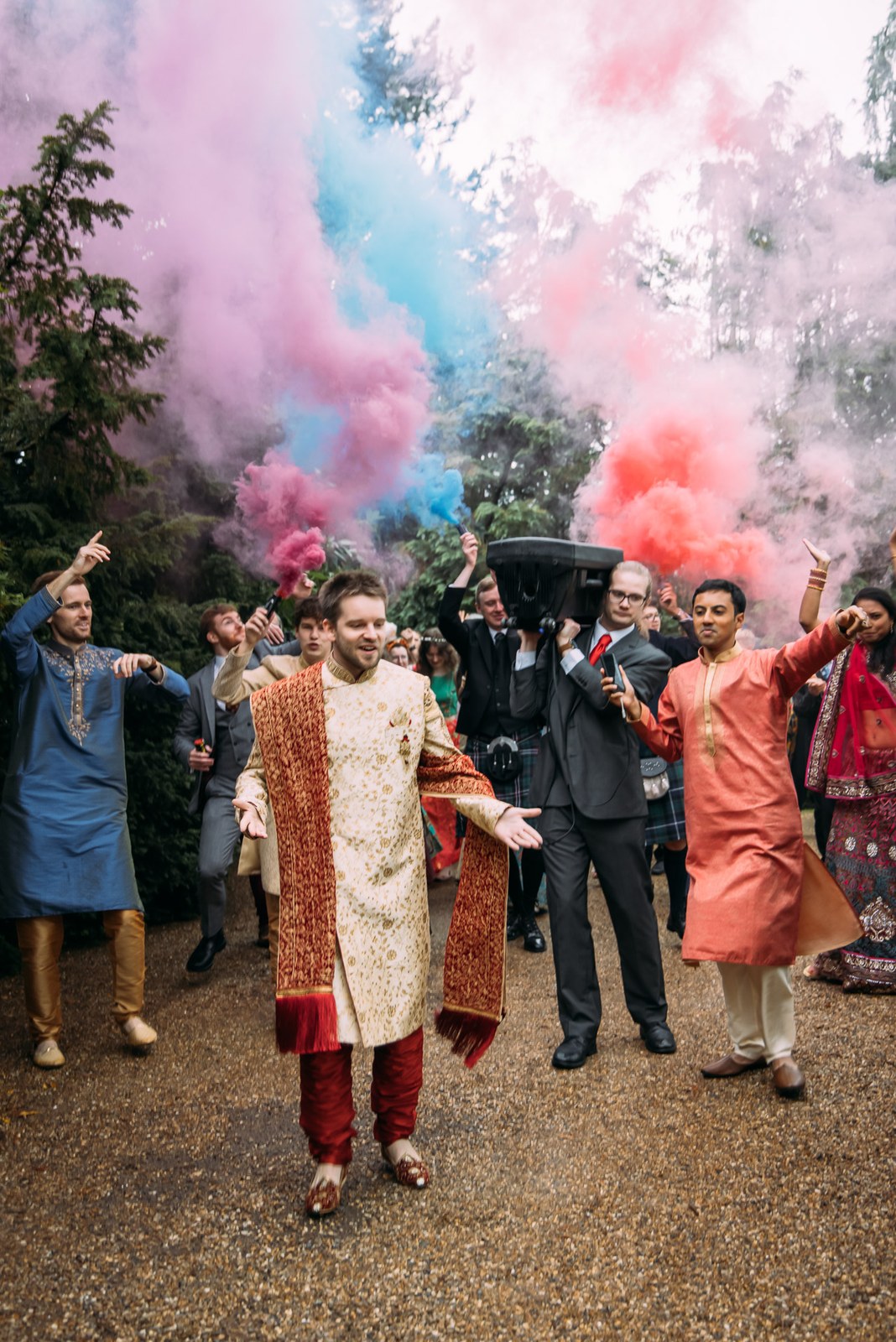 The groom leading his procession through pink and blue smoke as guests cheer