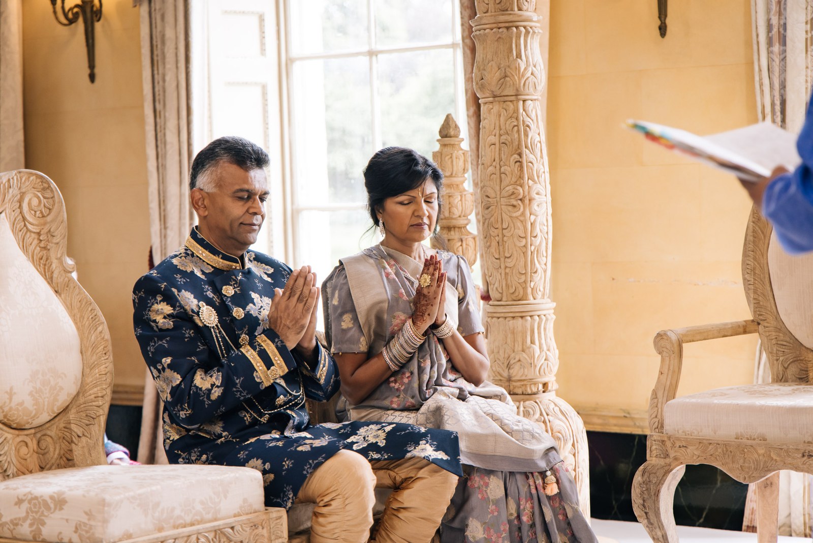 Two elders seated with palms pressed together in prayer during the ceremony