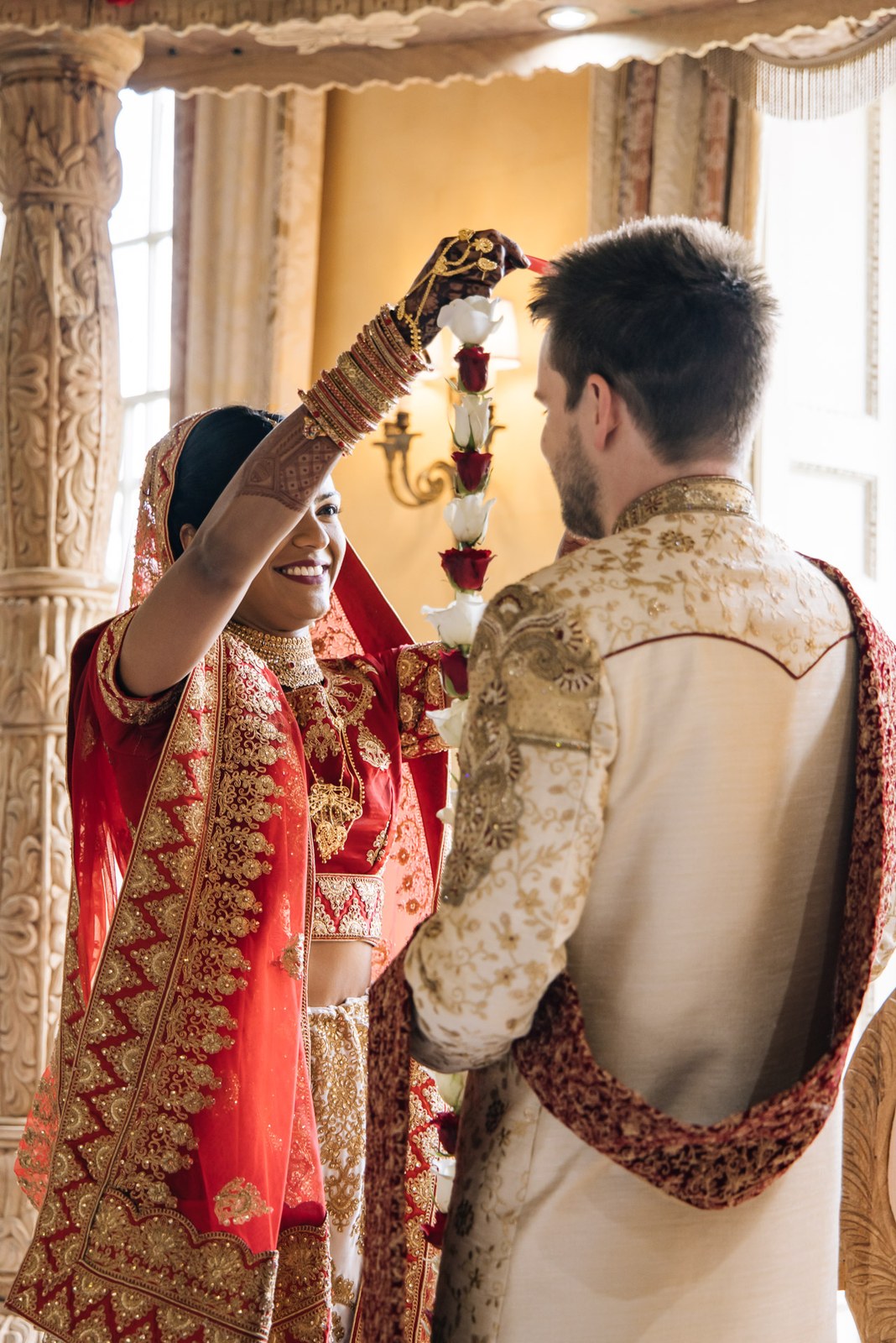 The bride raising a flower garland to place over the groom during the jaimala
