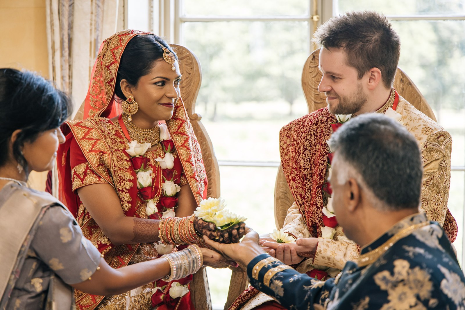 The couple seated as the bride holds a flower-topped coconut over an elder's palms
