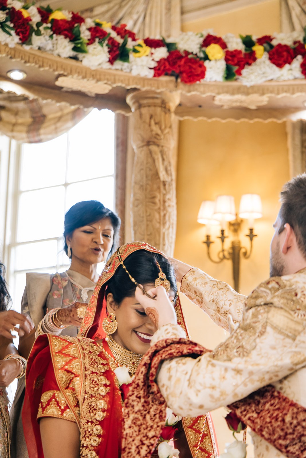 Bride laughing as the groom applies sindoor to her hairline
