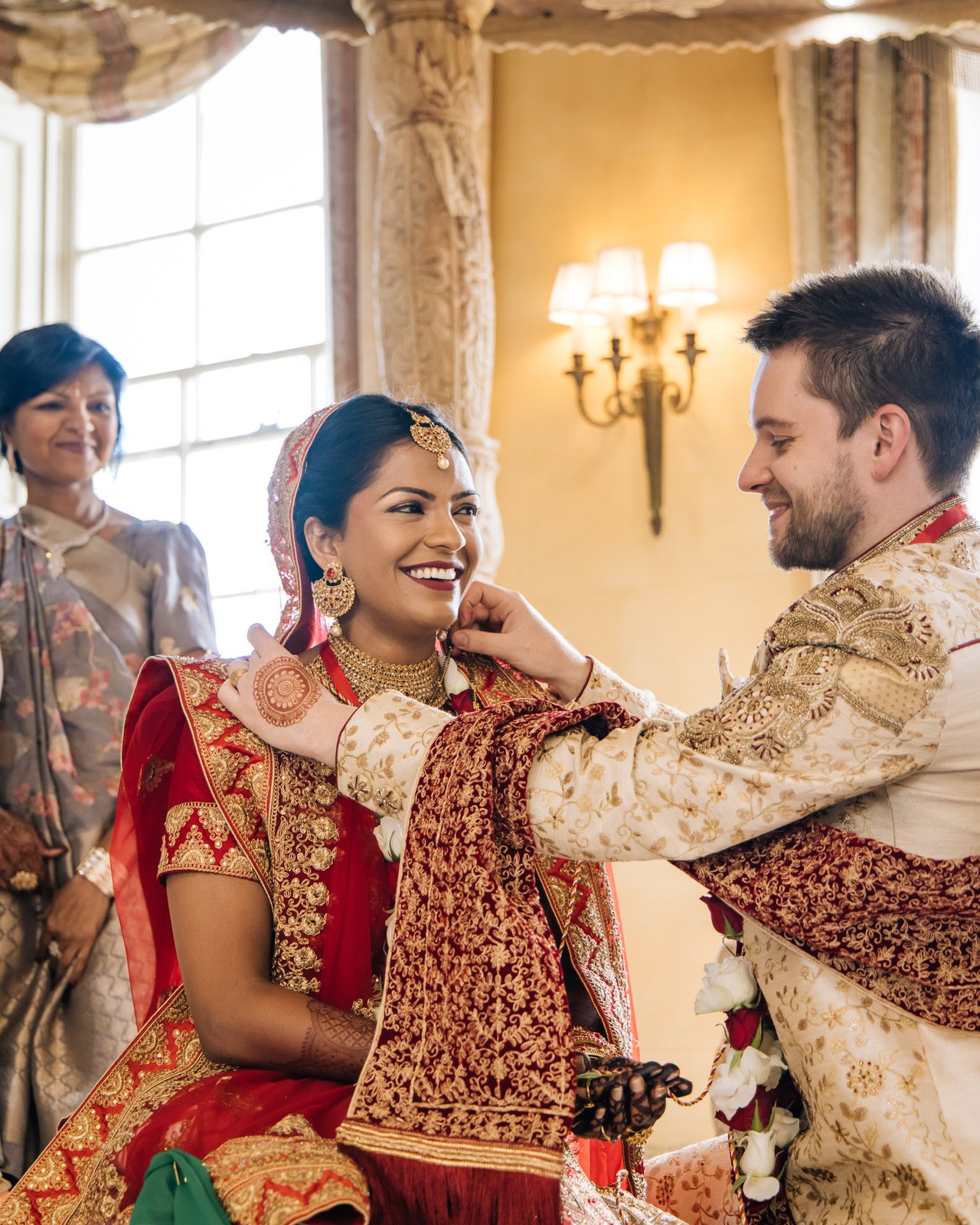 The couple seated beneath the rose-garlanded mandap with family beside them