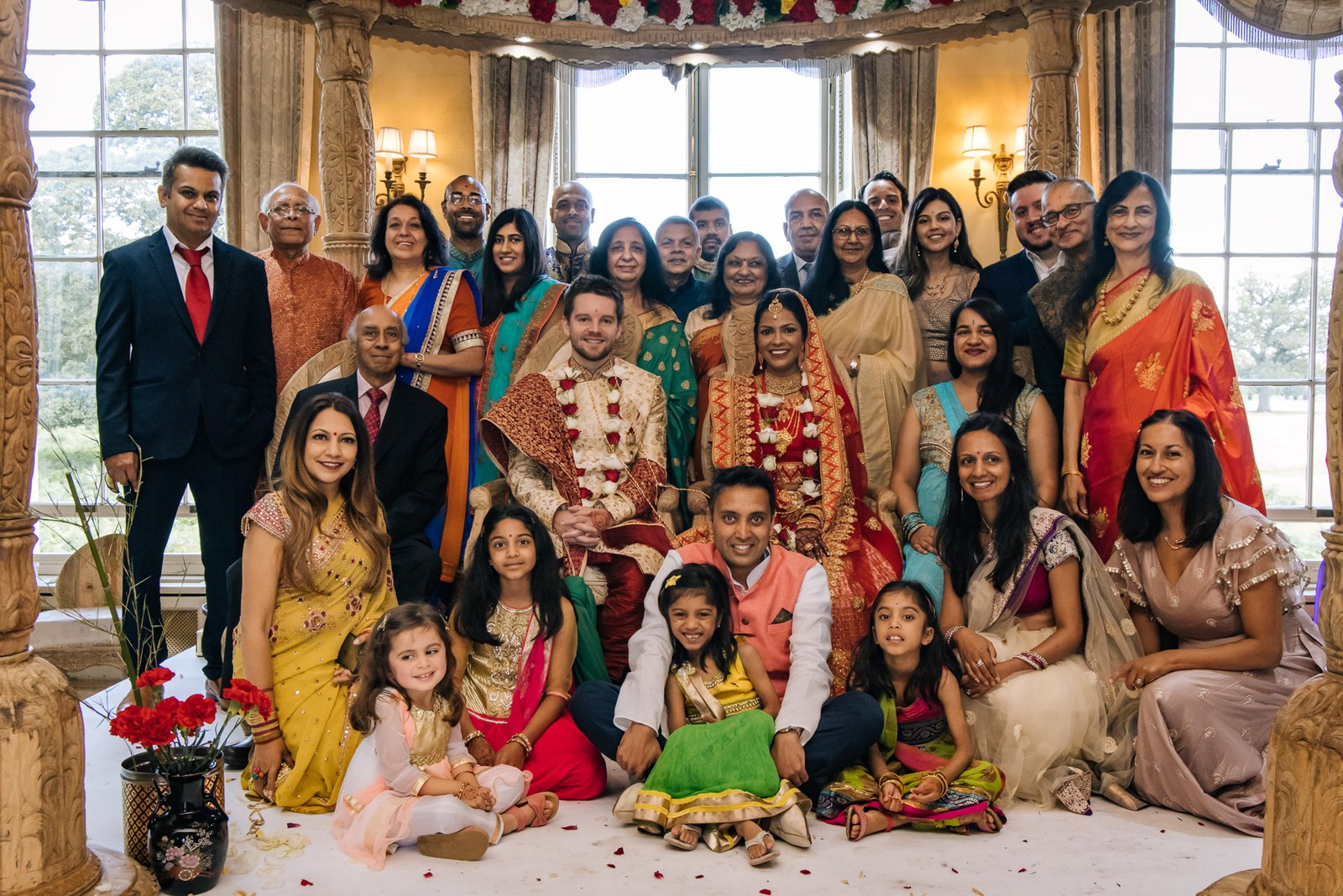 The full family group posed beneath the mandap in the bay-window room