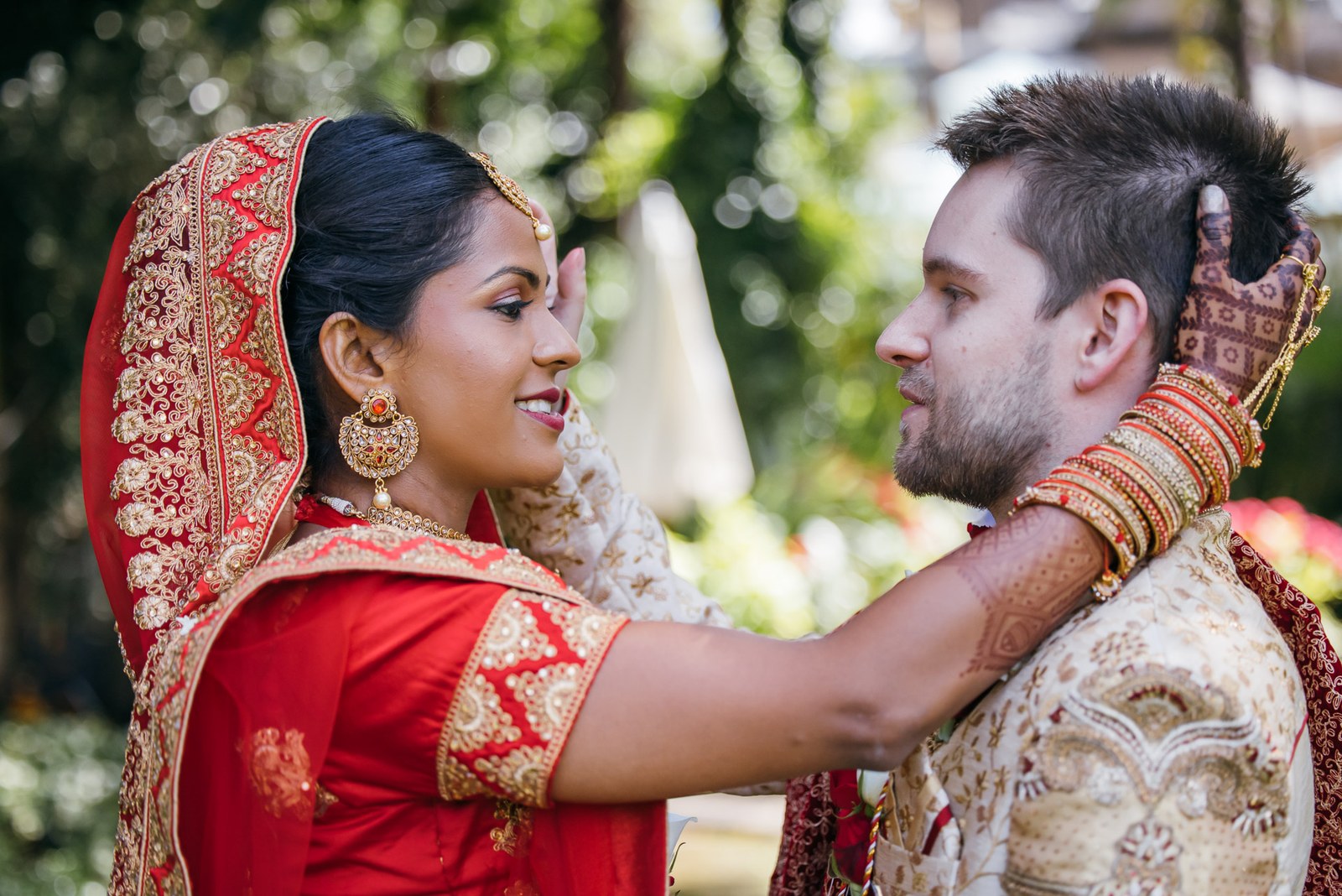 The bride tenderly adjusting the groom's face outdoors in the sunshine