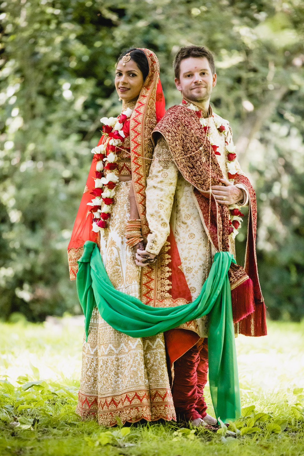 Full-length portrait of the couple on the lawn, her green dupatta trailing
