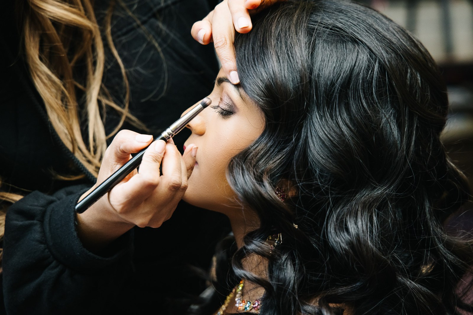 A make-up artist applying eye make-up to the bride before the reception