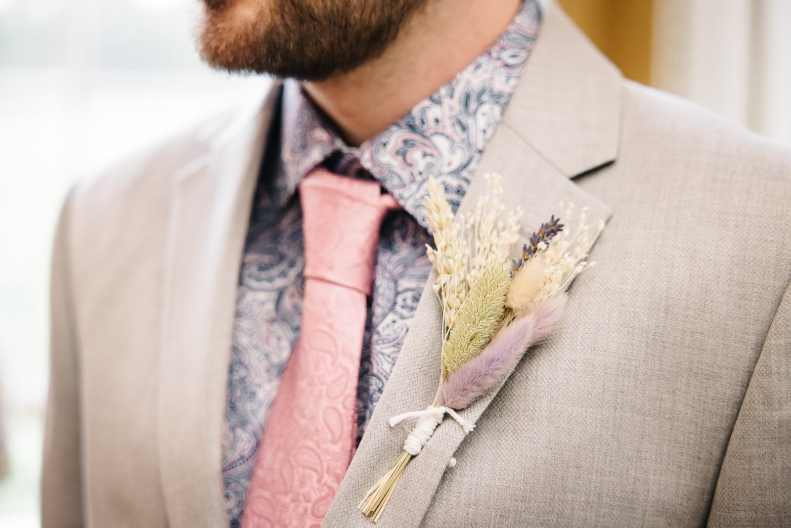 Close-up of the groom's beige suit, pink tie and dried-flower buttonhole