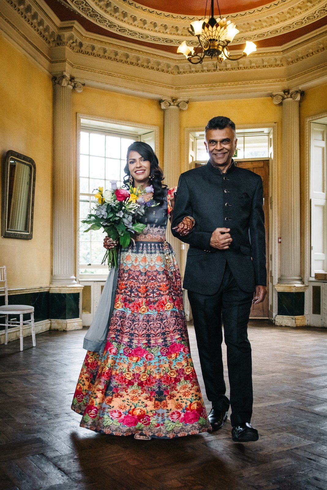 Bride in a vivid floral gown on her father's arm in the domed yellow room