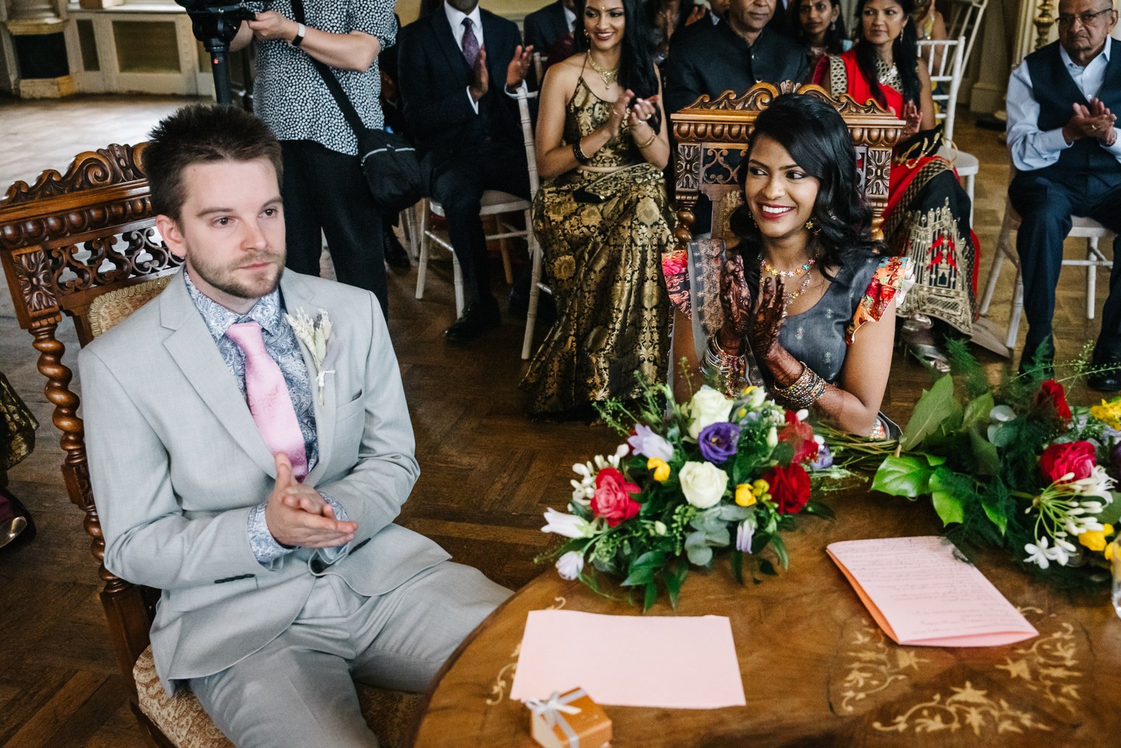 The groom seated at the flower-topped register table, the bride beside him