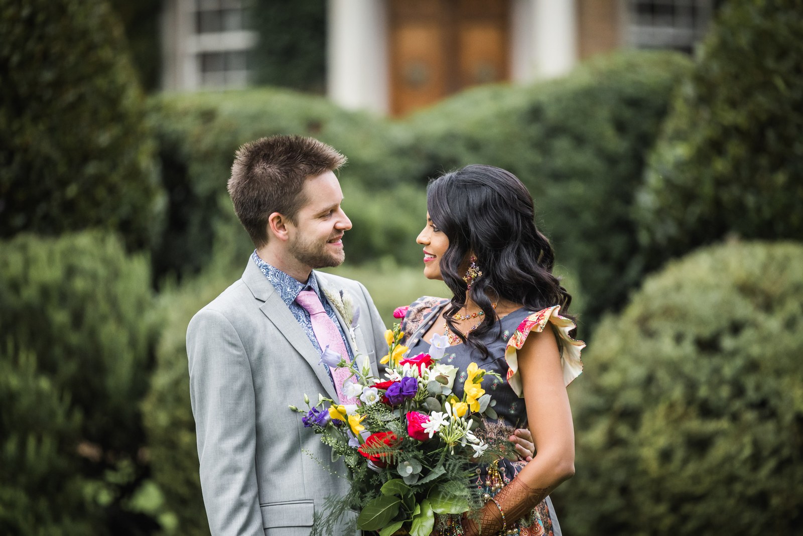 Bride and groom among the clipped topiary in the garden, bouquet in hand