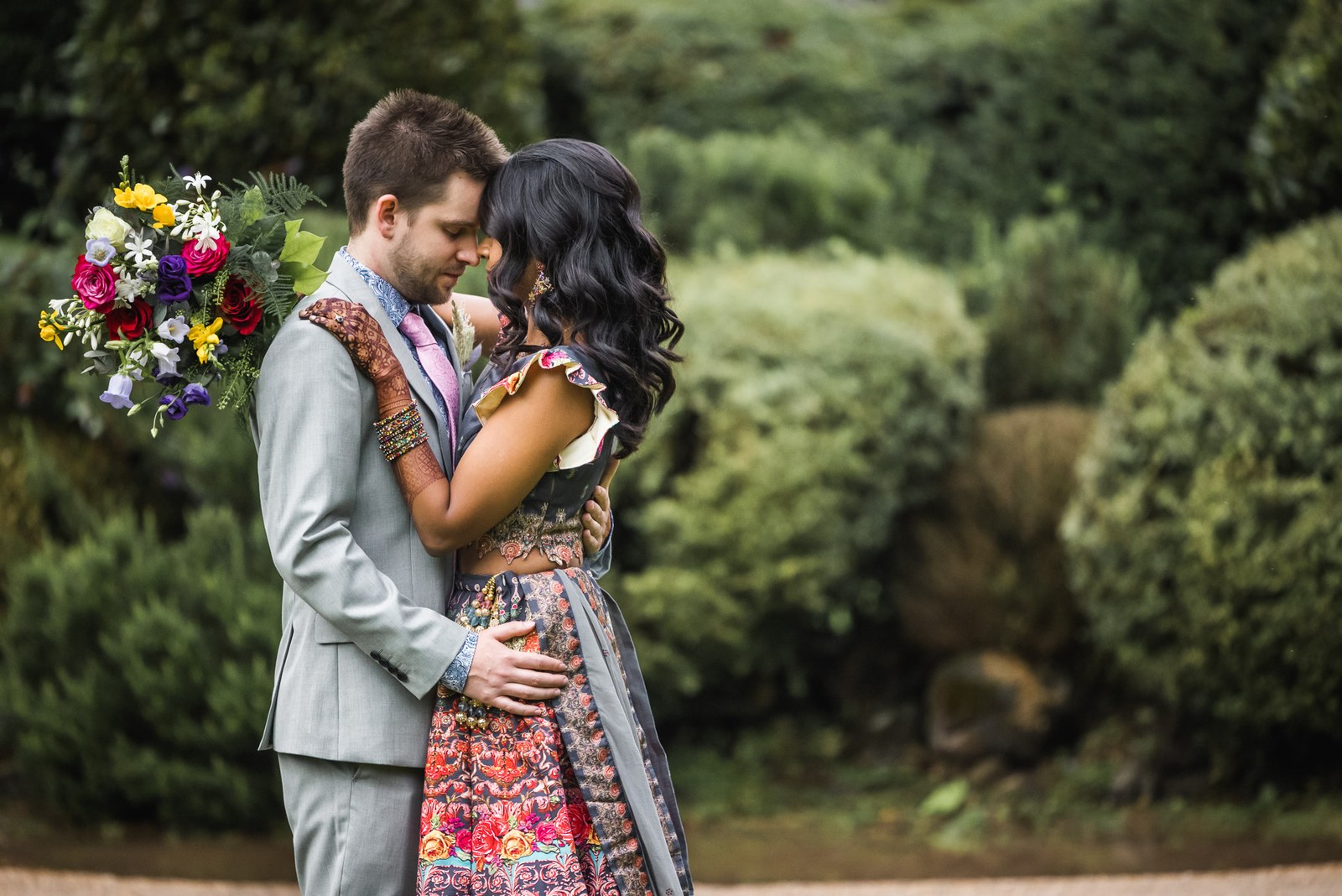 The couple embracing in the garden, the bride holding a bright bouquet