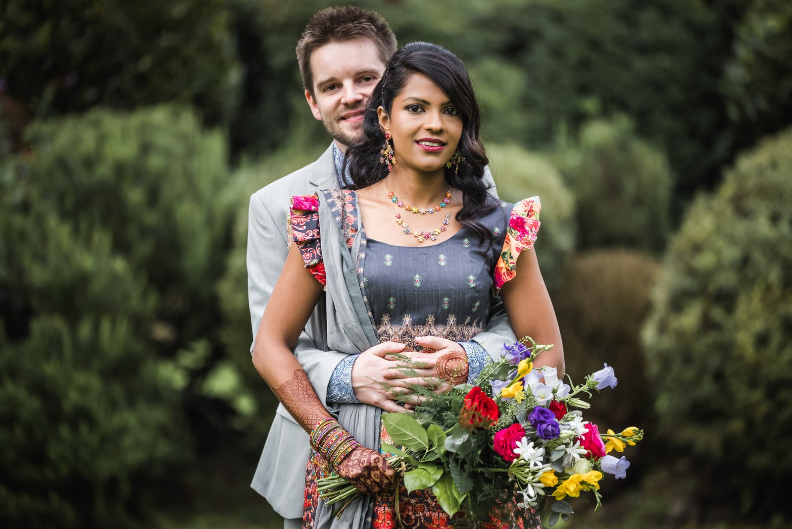 Bride and groom smiling in the garden with a colourful wildflower bouquet