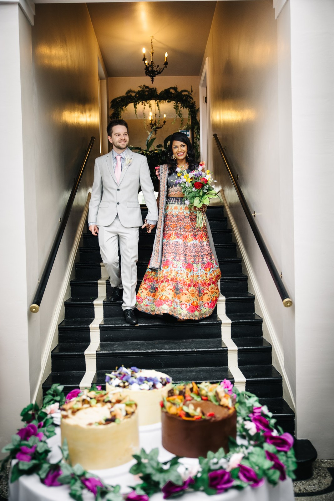 The couple descending the black staircase towards flower-ringed cakes