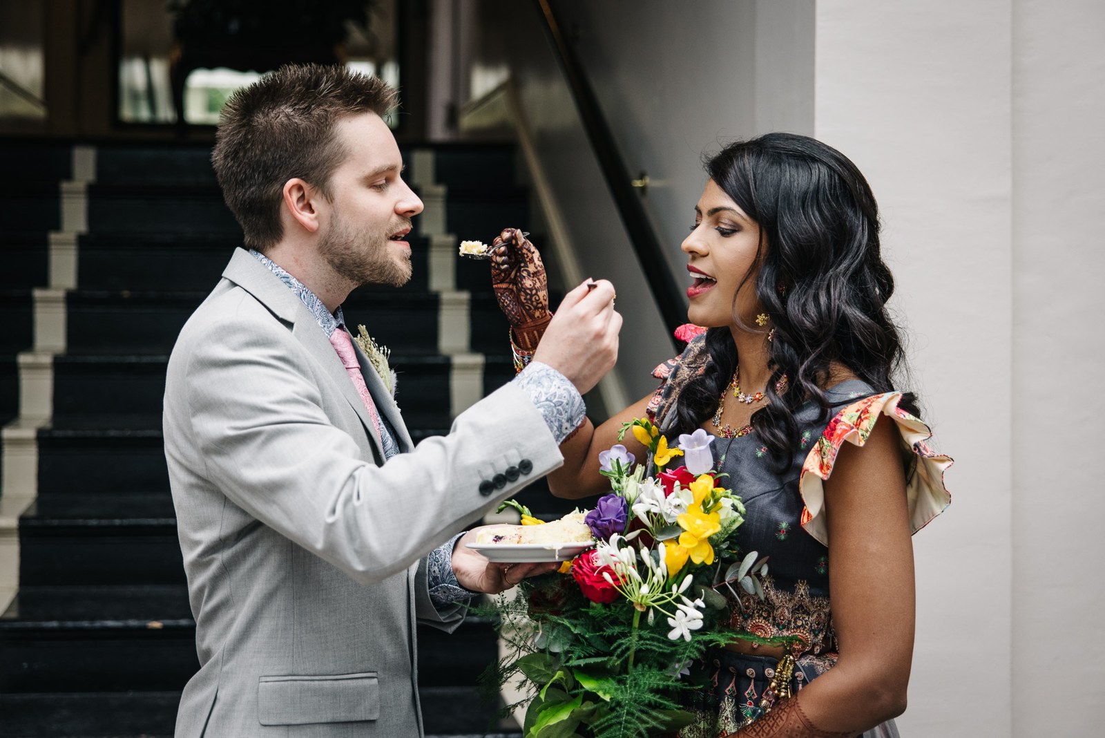 The groom feeding the bride a taste of cake beside the staircase